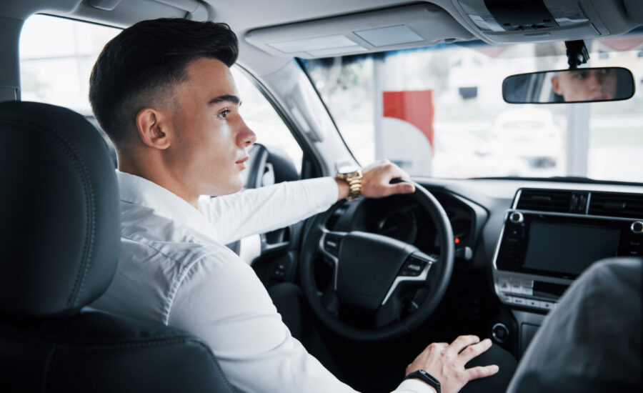 A young man in the driver's seat of a car listens to his instructor