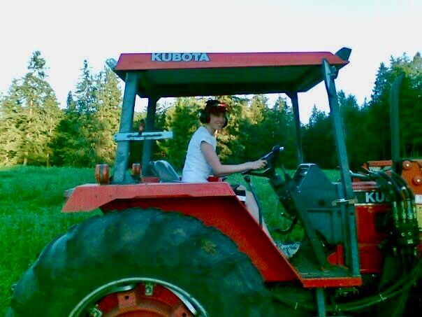 A woman at the wheel of an orange tractor in a forest