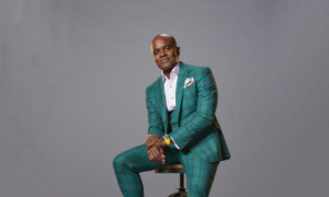 Canadian entrepreneur and Dragon's Den judge Wes Hall sits on a stool against a grey background, smiling.