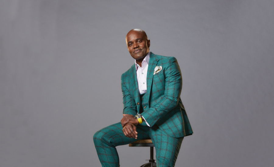 Canadian entrepreneur and Dragon's Den judge Wes Hall sits on a stool against a grey background, smiling.