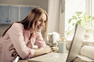 A young woman in a kitchen smiles at G I C returns on her laptop