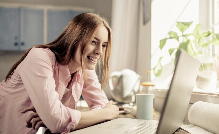 A young woman in a kitchen smiles at G I C returns on her laptop