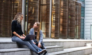 Two women sit on the steps of an office building, having a conversation