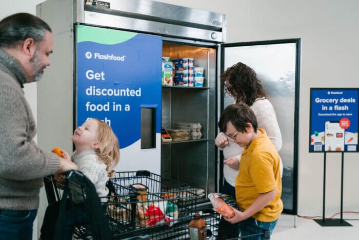 A family picks up discounted items from a Flashfood fridge in a grocery store.