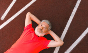 A man in his late 50s lies on a race track with his arms stretched behind his head