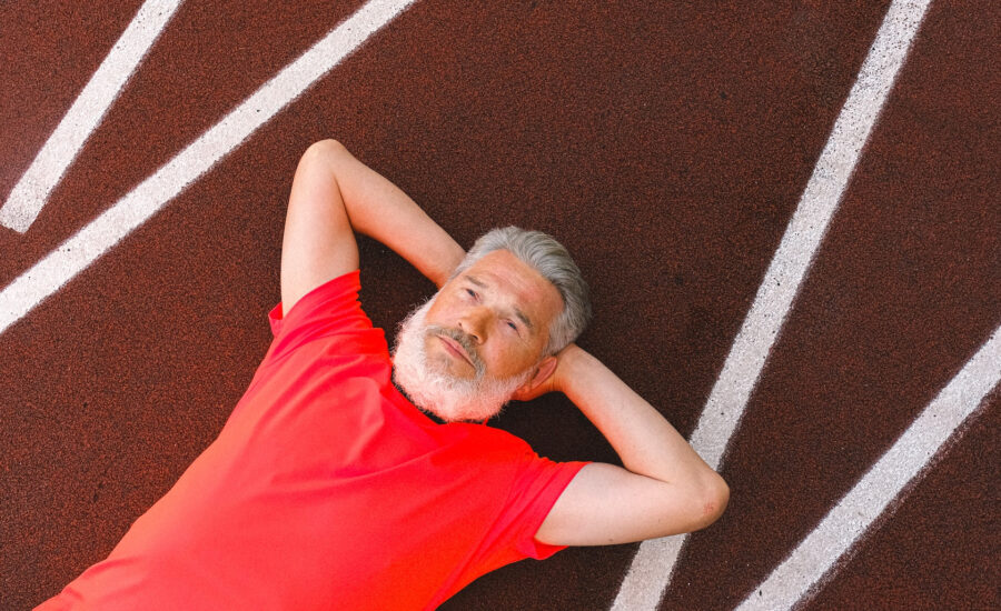 A man in his late 50s lies on a race track with his arms stretched behind his head