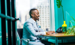 A man in a suit sits in his office typing at a keyboard