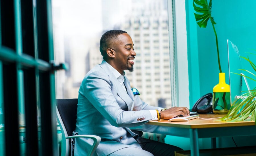 A man in a suit sits in his office typing at a keyboard