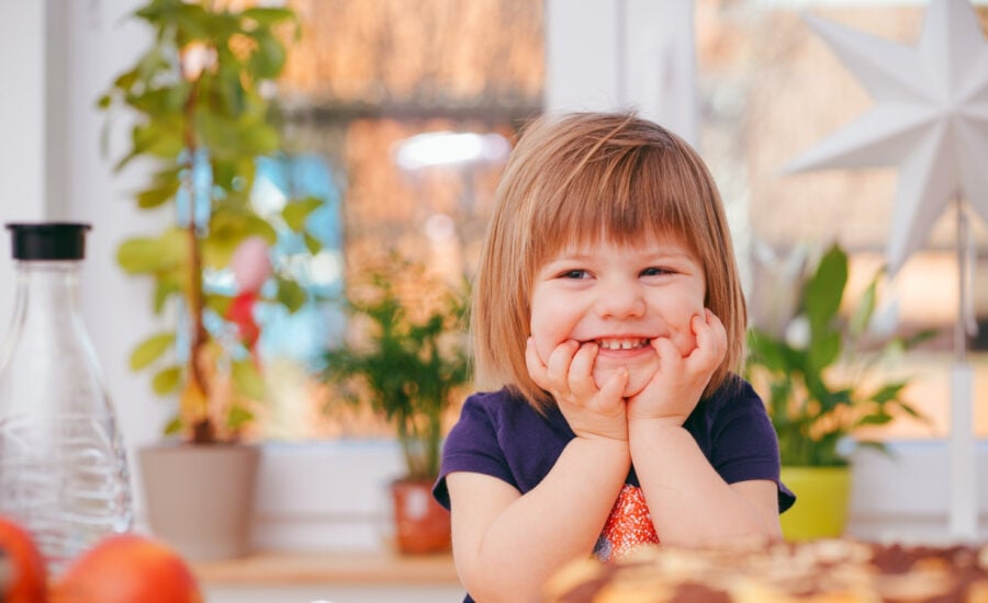 A smiling toddler holds her head with her hands