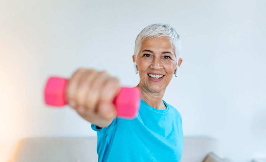 A smiling older woman lifting a small barbell