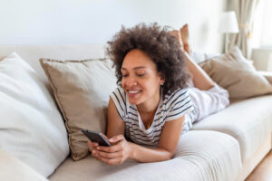 A woman lies on a sofa and smiles at GIC returns shown on her phone