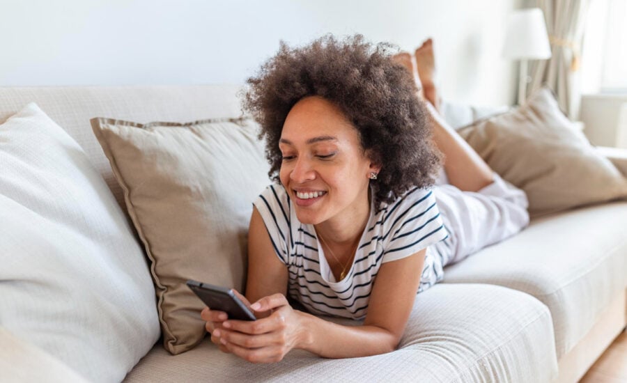 A woman lies on a sofa and smiles at GIC returns shown on her phone