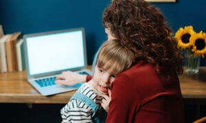 A mom sits at a computer with her toddler, looking at her investing accounts for her family as a result of emotional investing.