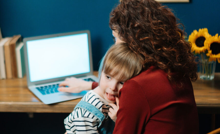 A mom sits at a computer with her toddler, looking at her investing accounts for her family as a result of emotional investing.