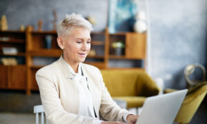 A middle-aged woman in a business suit works on her laptop