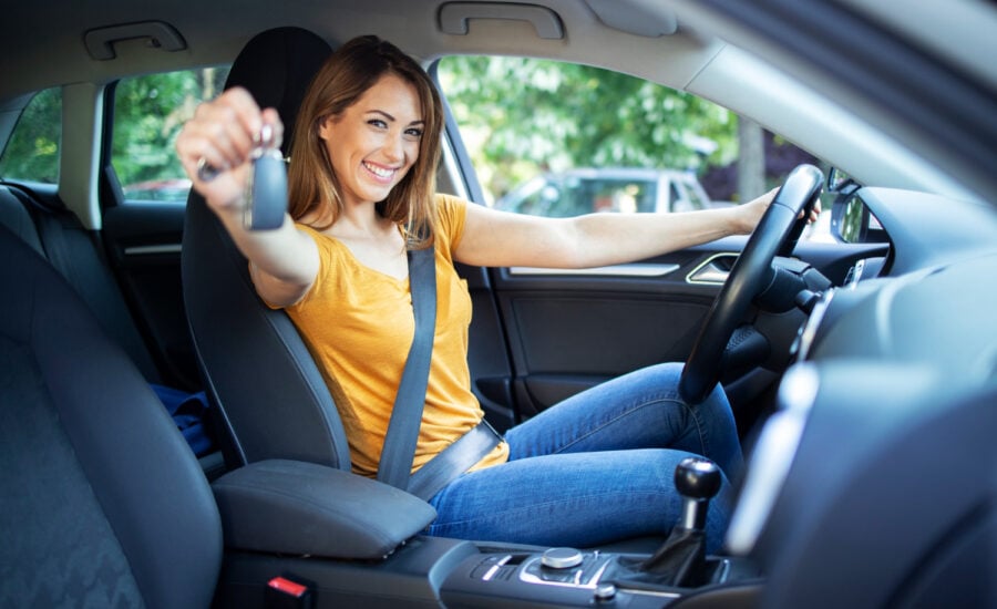 A smiling young woman driver holds out a set of keys