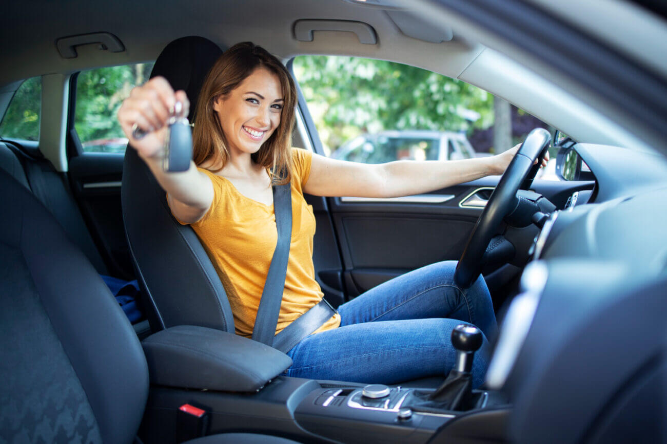 A smiling young woman driver holds out a set of keys