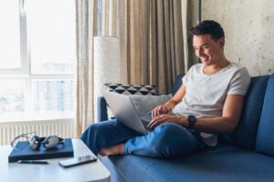 A young man sits on a sofa and buys GICs on his laptop