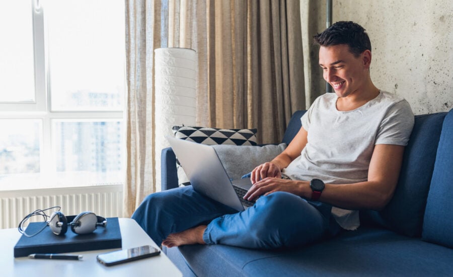 A young man sits on a sofa and buys GICs on his laptop