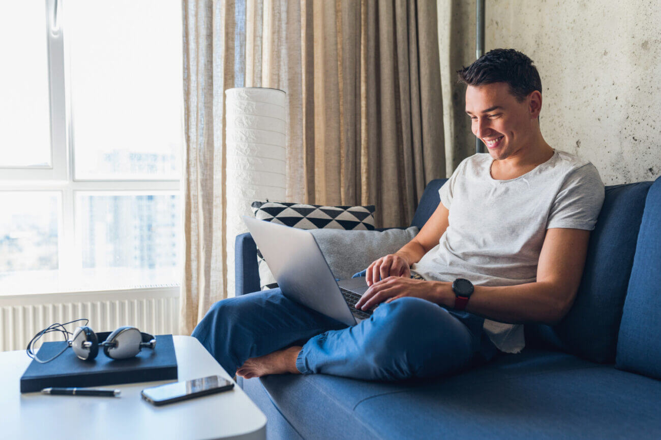 A young man sits on a sofa and buys GICs on his laptop
