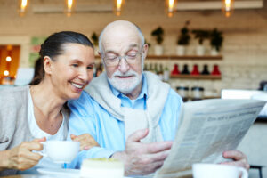 A smiling senior-age couple in a cafe discuss a newspaper article