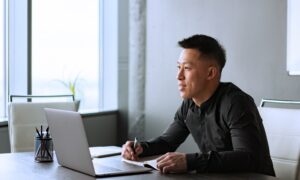 A middle-aged man takes notes about tech stocks from his laptop