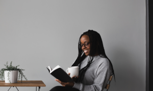 A woman sits against a grey wall reading a book on international women's day.