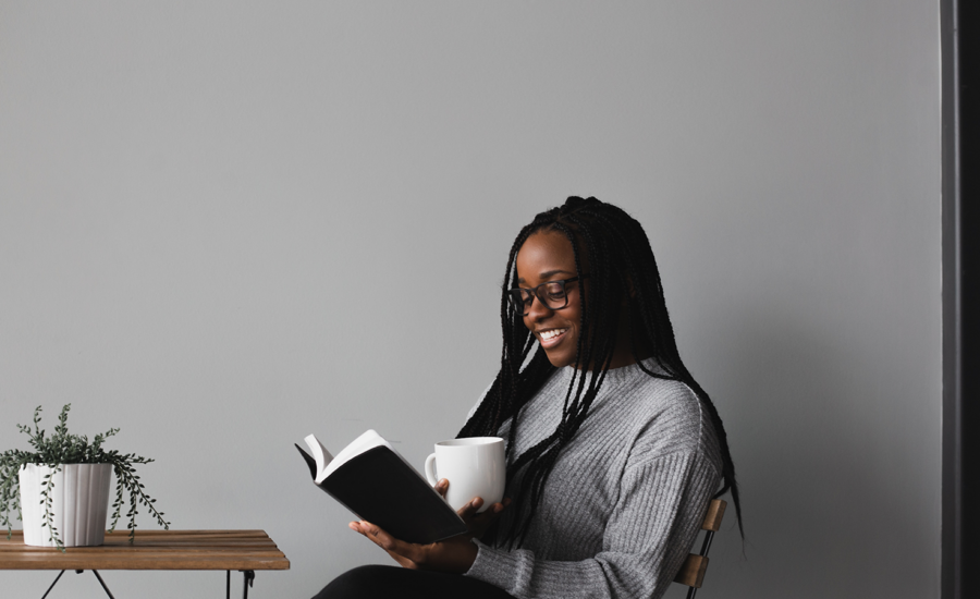 A woman sits against a grey wall reading a book on international women's day.