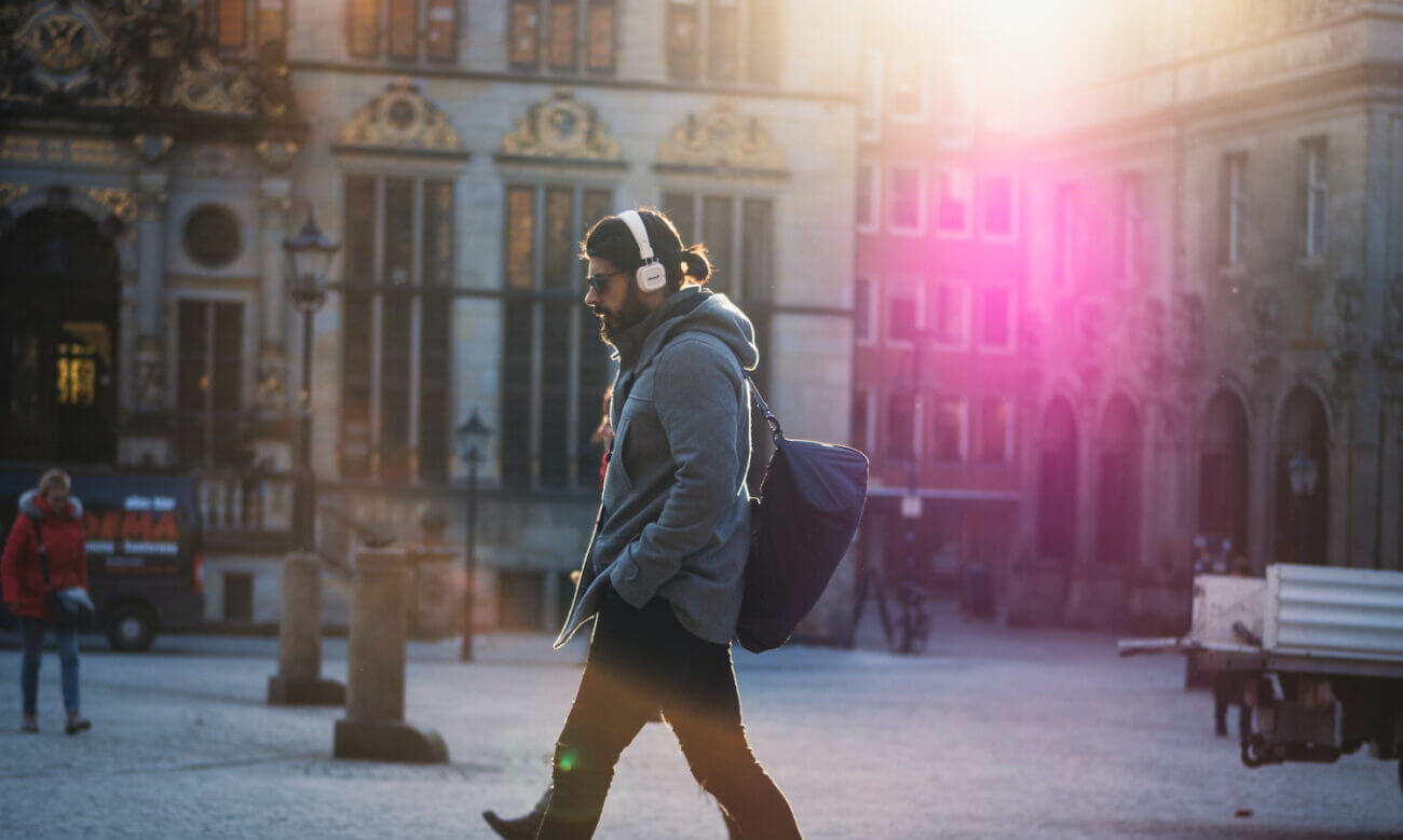 A man walks along a European street wearing headphones and carrying a bag