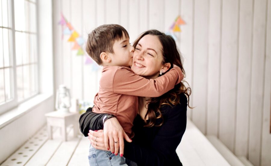 A woman hugs her young son in a sunlit room