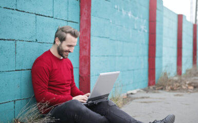 A man sits against a wall outside comparing FHSA rates online