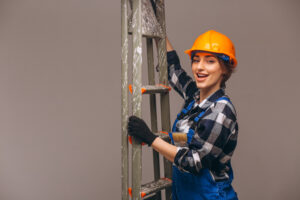 A smiling woman in work clothes holds a ladder