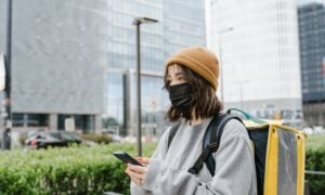 A woman working a side hustle in food delivery holds her phone and smiles.