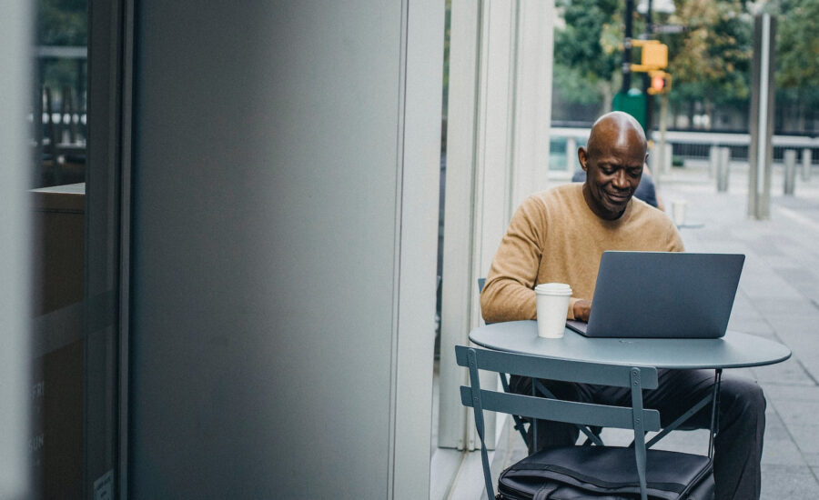 A man sits outside of a coffee shop, working on his laptop