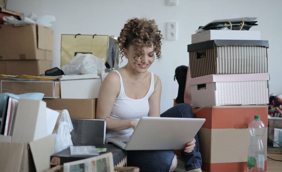 A woman sits on the floor, surrounded by boxes of her belongings, to illustrate how to make money selling stuff online.