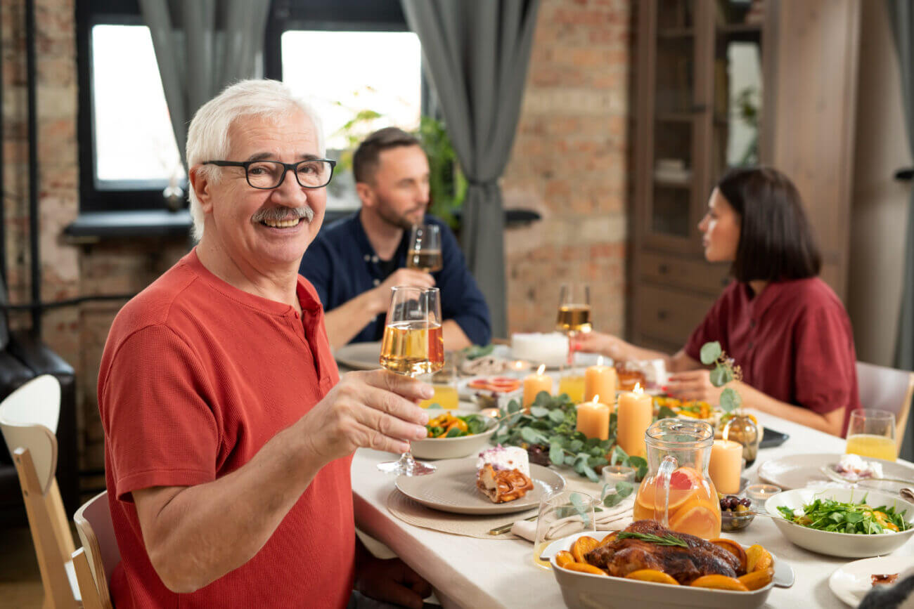 A smiling senior-age man at a dinner table with his adult son and daughter