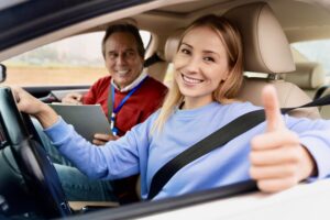 Smiling young woman sits beside a driving instructor in a car