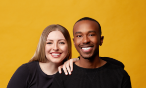 Steph Gordon and Dennis Mathu smile at the camera against a yellow background.
