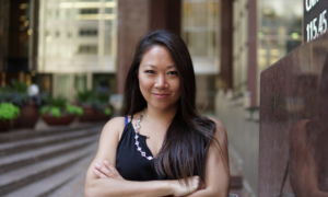 Financial planner Michelle Hung looks at the camera, smiling slightly with her arms crossed in front of office buildings.