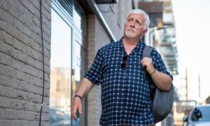 A man with a pensive expression walks down a street