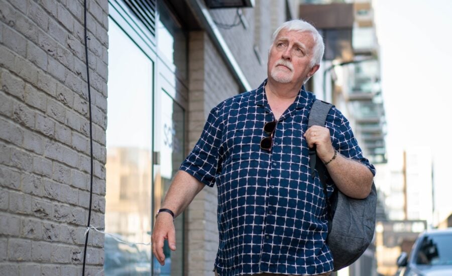 A man with a pensive expression walks down a street