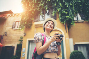 A young woman smiles and holds a camera on a charming street