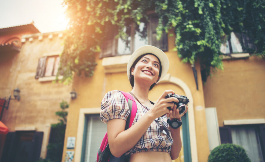 A young woman smiles and holds a camera on a charming street