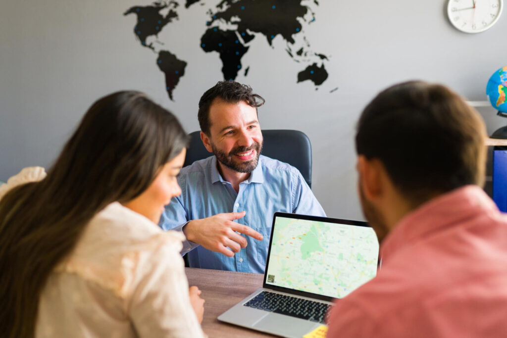 A travel agent smiles as he shows a map to a young man and woman