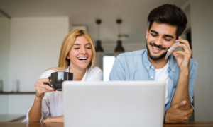 A man and woman smile and laugh while looking at a laptop screen.