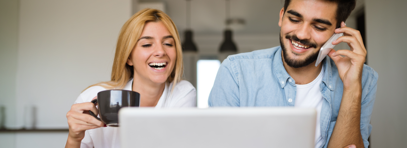 A man and woman smile and laugh while looking at a laptop screen.