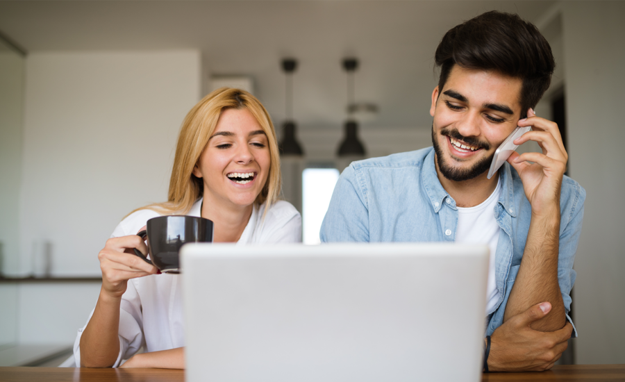 A man and woman smile and laugh while looking at a laptop screen.