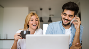 A woman (left) laughs while holding a cup of coffee and a man smiles while talking on the phone.