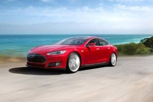 A red Tesla Model S drives along a coastline