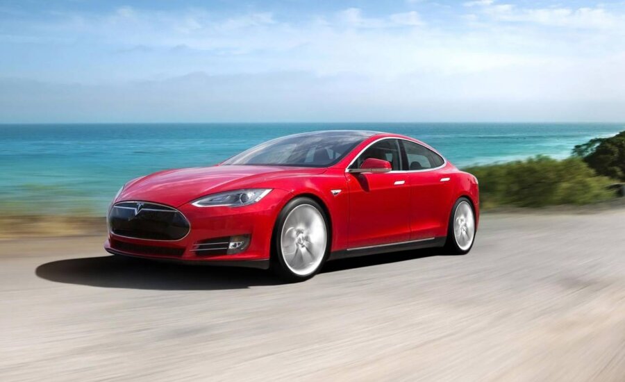 A red Tesla Model S drives along a coastline